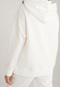 Hooded sweatshirt in light cream with a subtle pattern. Features a relaxed fit, ribbed cuffs, and a textured, smooth fabric.