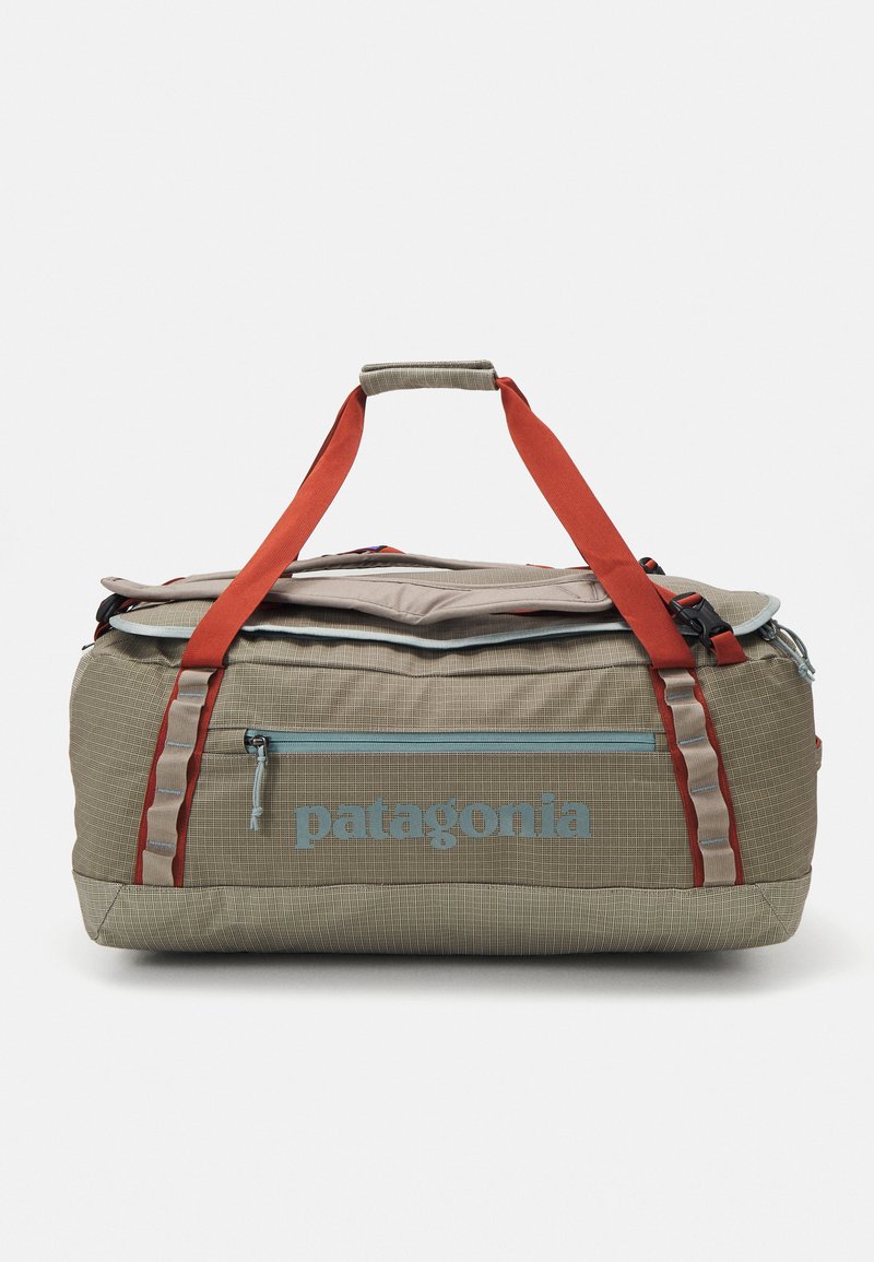 Duffle bag with a tan checkered pattern, red and blue accents, a top zipper, and a front pocket. Features dual handles for carrying.