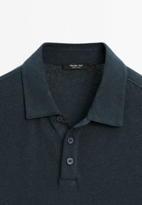 Mörkblå polo skjorta i strukturerad tyg med platt krage, tre-knapplist och en etikett i halsringningen.