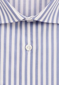 Col et zone de boutons d'une chemise blanche avec des rayures verticales bleu clair en largeurs alternées et une texture en chevrons.