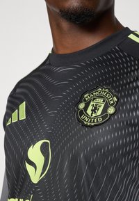 Schwarzes Fußballtrikot mit strukturiertem Muster, mit neon-grünen Akzenten, Rundhalsausschnitt und dem Emblem von Manchester United.
