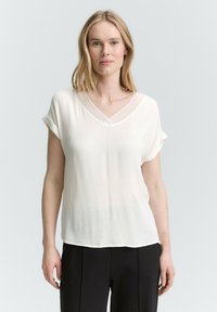 Biała bluzka z krótkim rękawem z dekoltem w serek, wykonana z lekkiego materiału, z podwiniętymi rękawami; gładka tekstura z eleganckim układem.