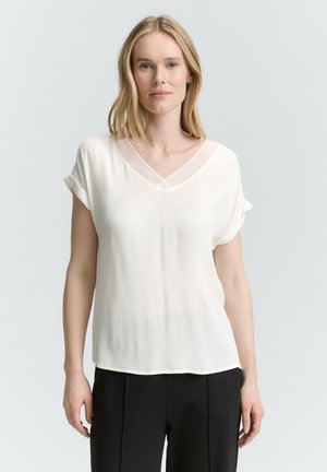 Bílá blůza s krátkým rukávem a výstřihem ve tvaru V, z lehkého materiálu a s ohrnutými rukávy; hladký povrch s elegantním splýváním.