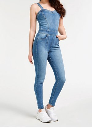 Vaaleansininen farkkuhaalaripuku, jossa on istuva yläosa olkaimilla, korkea vyötärö ja kapenevat lahkeet. Kaksi etutaskua lisää käytännöllisyyttä.