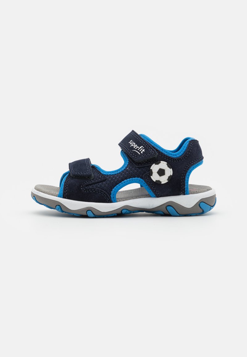 Sandalias azules y marinas con un acento de balón de fútbol, hechas de tela y goma, con dos correas de Velcro y una suela acolchada.