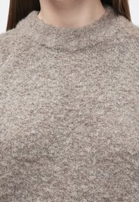 Beige stickad tröja med texturerad yta och hög hals, tillverkad av mjukt, fluffigt material. Inga mönster eller detaljer syns.