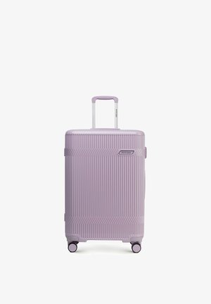 Valise rigide lavande à nervures verticales, équipée de quatre roues pivotantes et d'une poignée télescopique déployée, étiquette de marque visible à l'avant.