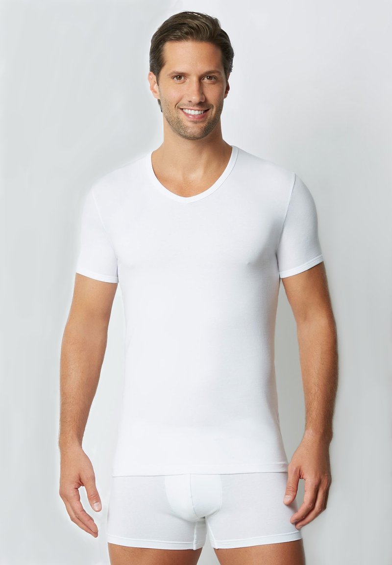 T-shirt bianco a maniche corte e scollo a V realizzato in tessuto morbido, abbinato a boxer bianchi aderenti, indossato da un modello maschile su uno sfondo neutro.