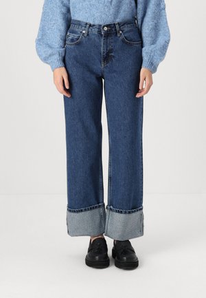 Wijd uitgesneden denim jeans in donkerblauw, met een geruit patroon op de boorden. Het materiaal is zacht, met zichtbare stiksels en zakken.