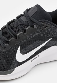 Schwarzer Sportschuh mit einer strukturierten Mesh-Oberfläche, weißem Nike-Swoosh-Logo, grauen Akzenten und einer gepolsterten Sohle, die mit "AIR" beschriftet ist.