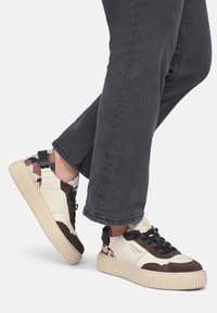 Sneaker con una combinazione di crema, marrone e motivi di camouflage, dotate di suola in gomma, lacci neri e un tallone imbottito.