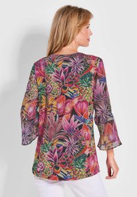 Bloes met bloemenpatroon in doorzichtig stof, met levendige kleuren zoals roze, groen en goud, met klokmouwen en een losse pasvorm.