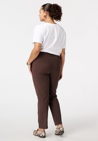 Pantalons marron à coupe ajustée, avec poches avant et finition en tissu lisse. Associés à un t-shirt blanc et des ballerines à motif.