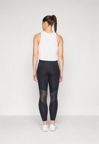 Leggings noirs avec des panneaux en maille et une large taille, associées à un débardeur blanc à côtes. La coupe est près du corps, idéale pour les activités physiques.