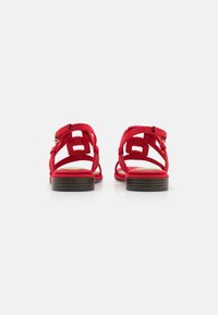 Sandales en suède rouge avec un design de sangles entrecroisées, un petit talon et une fermeture à boucle réglable sur une semelle en bois brun.