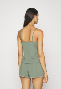 Olivenfarbene Schlafanzugset mit einem enganliegenden Top mit dünnen verstellbaren Trägern und Spitze, kombiniert mit locker sitzenden Shorts.