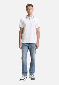 Hvid bomulds polo skjorte med en blå detalje på kraven, parret med lyseblå jeans og sorte og hvide sneakers.