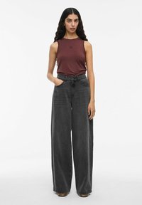 Burgunderfarbener ärmelloser Oberteil mit kleinem Logo; weit geschnittene schwarze Jeans mit hoher Taille und Fronttaschen. Glatter Stoff und lockere Passform.