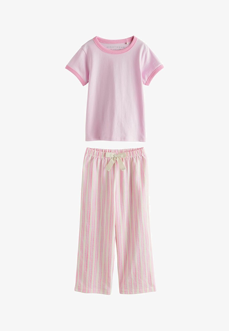 Jasnoróżowy top z krótkim rękawem połączony z białymi luźnymi spodniami z pionowymi różowymi paskami i beżową kokardą ze sznurkiem w talii.