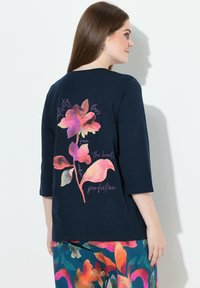 Navyblaues Langarmshirt mit einem bunten Blumendesign und Text auf der Rückseite; glatter Stoff, rundes Dekolleté und dreiviertellange Ärmel.