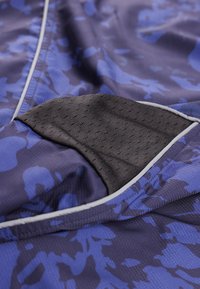 Κοντινό πλάνο υφάσματος μπλε και μαύρης καμουφλάζ με μαύρο υφασμάτινο έμπλαστρο με υφή και λευκή λεπτομέρεια σε αθλητική ενδυμασία.