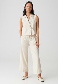Lichtbeige mouwloos vest met een enkele knoop, gecombineerd met wijde broekspijpen, gemaakt van zachte stof, met een trekkoord in de taille en opgerolde boorden.