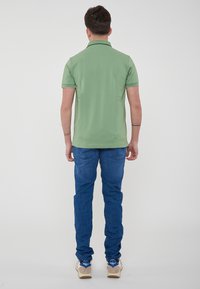 Polo shirt in cotone verde con maniche corte, dotato di colletto e rifiniture verde scuro. Indossato con jeans in denim blu e sneaker beige.