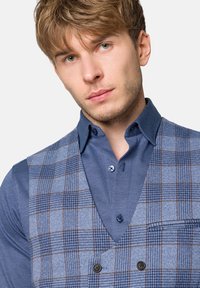 Niebieski kamizelka w kratę o gładkiej fakturze i kontrastowej niebieskiej koszuli, z guzikami i detalem kieszeni. Wzór zawiera cienkie brązowe linie.