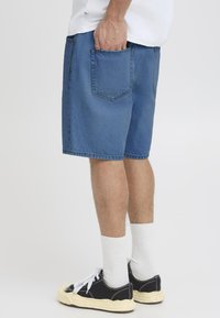 Zila denim šorti ar brīvu piegriezumu, redzamām šuvēm un aizmugurējo kabatu. Kopa ar melniem sporta apaviem un baltām zeķēm līdz potītei.