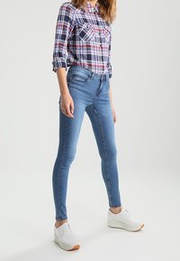 Ljust blå smala jeans med en slät yta, tillsammans med en rutig skjorta i röd, blå och vit färg, samt vita sneakers med gummisula.