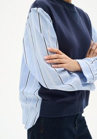 Felpa blu navy con maniche in tessuto a strisce azzurre. Le maniche hanno sottili strisce nere e bianche e un collo a coste.