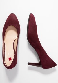 Burgundy mockaskinn högklackade skor med spetsig tå och en slät, mjuk yta. Sulan har en liten röd detalj på insidan.