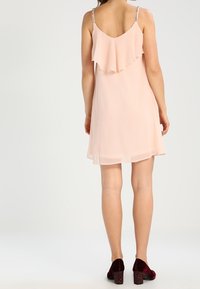 Světle růžové bezramínkové šaty s volánkovým detailem na zadní straně, do délky kolen, vyrobené z splývavé látky, v kombinaci s bordovými botami na blokovém podpatku.
