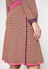 Robe en tricot présentant un motif à carreaux multicolores dans les tons rose, jaune et bleu foncé. Accent rose uni sur les poignets et l'ourlet. Silhouette évasée.