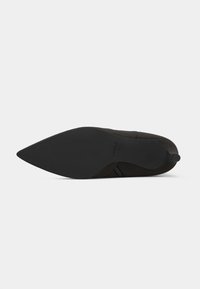 Sapato preto de bico fino com parte superior em tecido liso, sola texturizada e uma discreta alça na parte de trás. Design elegante e aerodinâmico.