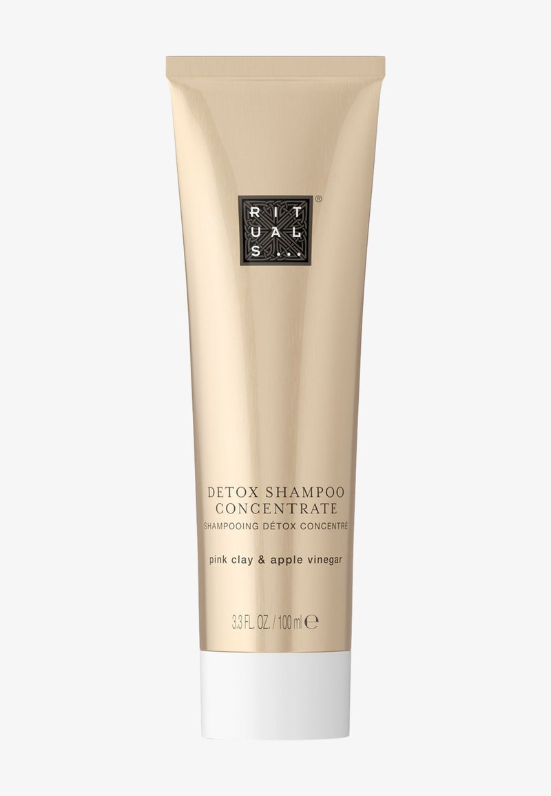 Kultainen metallinen shampoo-putki, joka on merkitty "Detox Shampoo Concentrate", mustalla logolla, valkoisella taittopullolla ja tekstillä, joka kuvaa ainesosia.