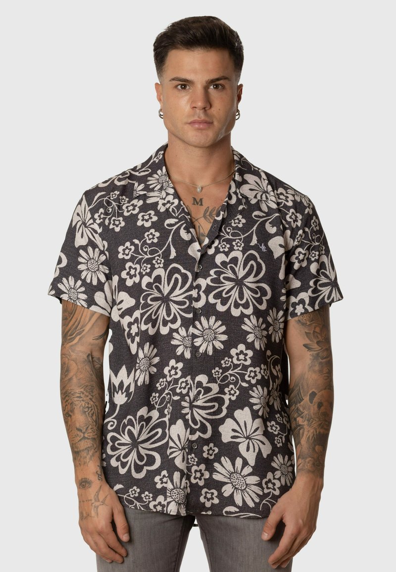 Camisa de botonadura de manga corta con un fondo oscuro y grandes patrones florales en blanco, de corte relajado, hecha de una tela ligera.