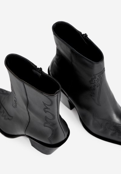 Black leather ankle boots with a low heel, featuring decorative stitching and a smooth texture. Zipper closure for easy wear.