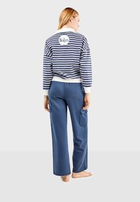 Prugasta tamnoplava i bijela dukserica s logom "The Beatles" na leđima, u kombinaciji s plavim cargo hlačama. Ležeran, opušteni kroj.