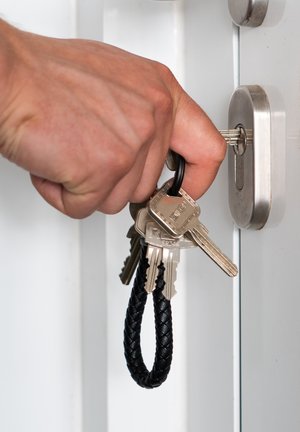 Keyring with several silver keys attached to a black braided leather loop, held by a hand near a silver door lock.