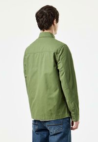 Grøn skjorte med knapper lavet af bomuld, med lange ærmer, krave og lige kant. Båret med blå jeans.