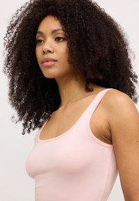 Lichtroze tanktop van zachte stof, met een ronde halslijn en dunne bandjes. Glad oppervlak met minimale stikseldetails.