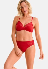 Ensemble de lingerie rouge comprenant un soutien-gorge avec des détails en mesh et des bretelles réglables, accompagné de culottes taille haute assorties avec des accents transparents.