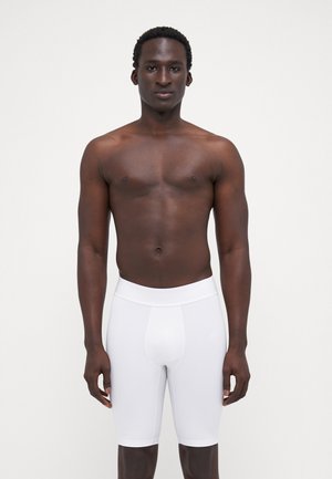 Vita tätsittade sportshorts med en slät yta och elastisk midja, bärs av en modell med ett neutralt uttryck.