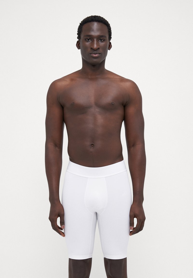 Hvide tætsiddende atletikshorts med en glat overflade og elastisk talje, båret af en model med en neutral ansigtsudtryk.
