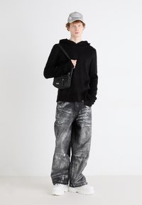 Um moletom de malha preto, jeans cinza de corte largo com manchas brancas e ténis brancos; acessorizado com uma pequena bolsa preta e um boné cinza.