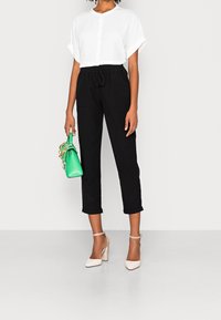 Biała button-up koszula o cropped fasonie, czarne spodnie ze sznurkiem, zielona torebka i beżowe szpilki z kostką, charakteryzujące się gładką fakturą tkaniny i prostym wzornictwem.