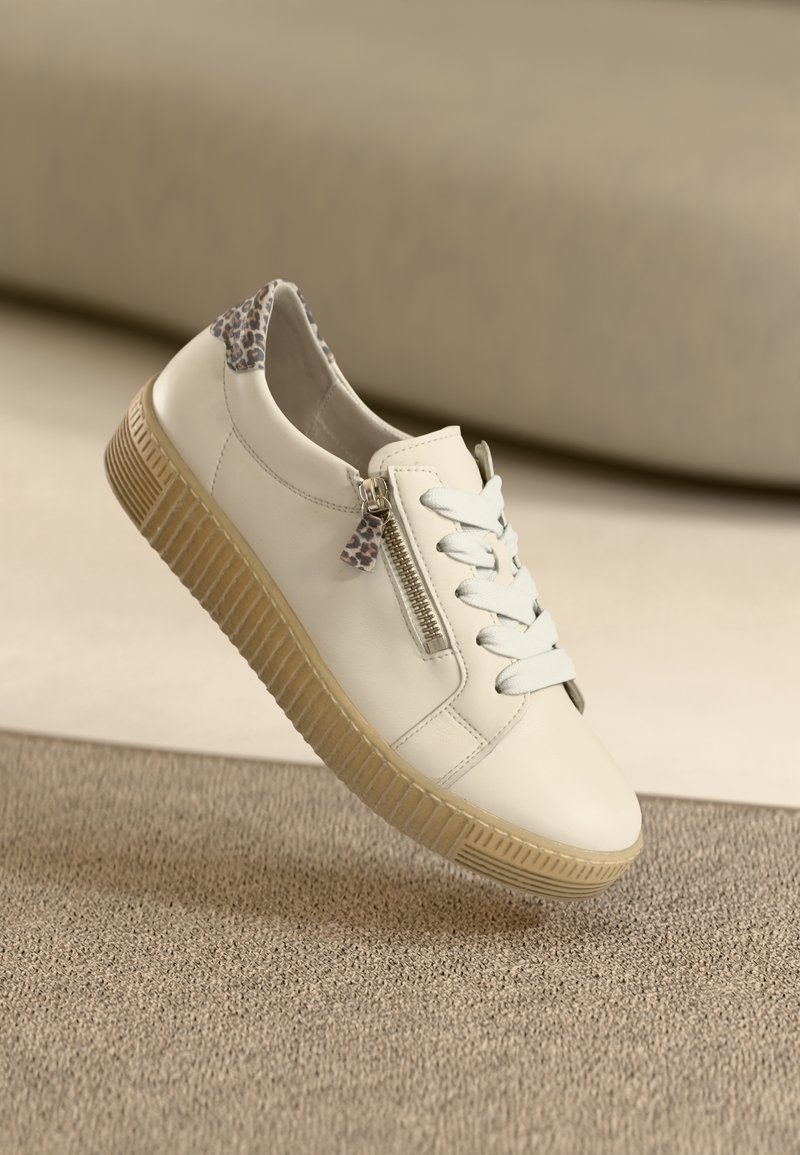 Valge nahast toss, beežist kummist tald, tasased paelad, külgmine tõmblukk ja leopardimustriga detail kandadel. Tekstuuriga kangast taust.