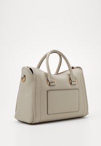 Beżowa skórzana torebka z dwoma zaokrąglonymi uchwytami, usztywnionym kształtem, bocznymi szwami i prostokątną łatą po jednej stronie. Złote elementy ozdobne.