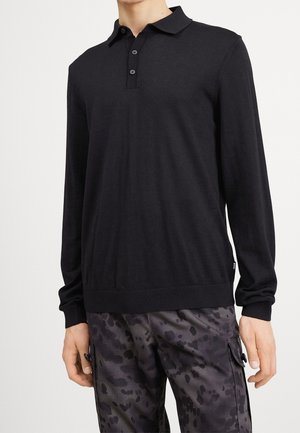 Homme portant un polo noir à manches longues associé à un pantalon cargo camouflage noir et gris.